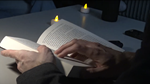 zwei Hände halten ein Buch mit Kerzen im Hintergrund